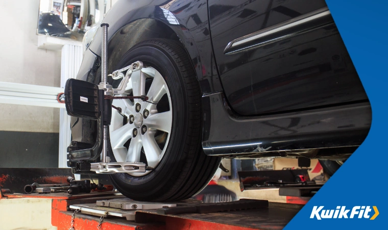 Wheel alignment check being performed on a vehicle in a garage.