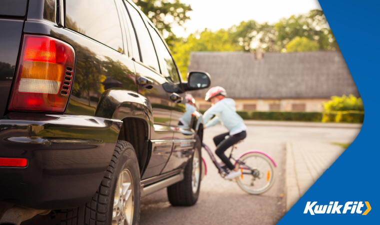 A kid cycling on a bike in front of a car.