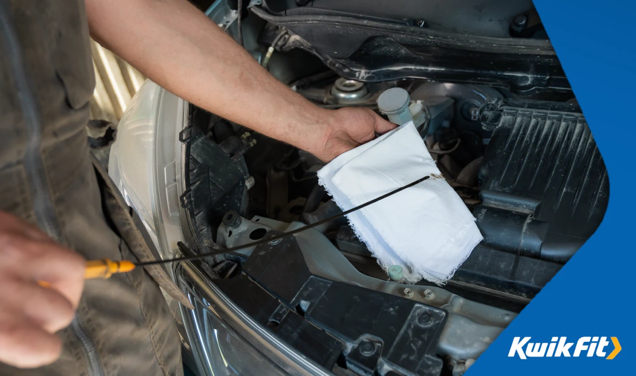 Person cleaning an oil dipstick with a white cloth.