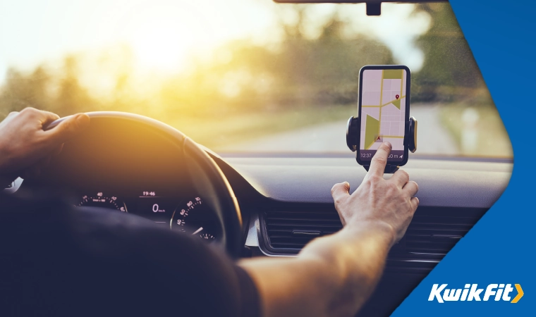 Person with one hand on the wheel driving while the other hand is pressing a map on a phone screen.