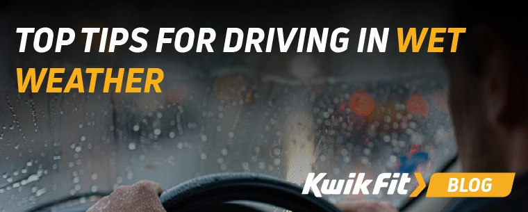 Person holding steering wheel looking out of rain covered windshield.