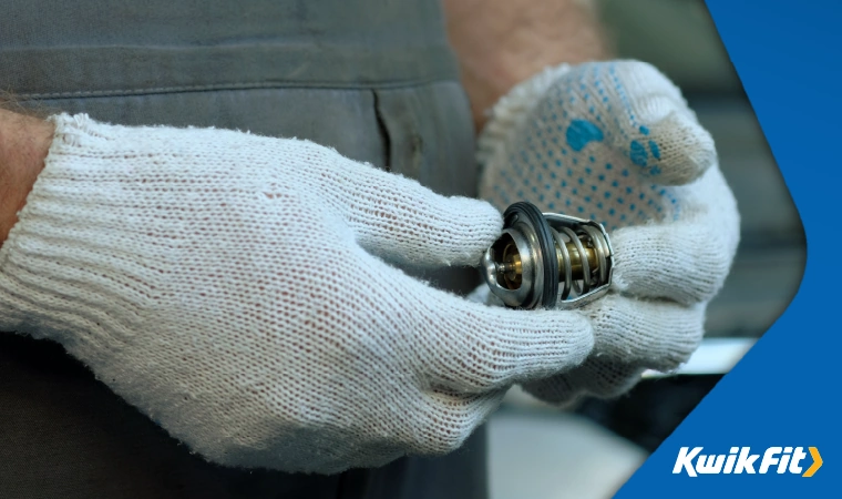 Technician wearing white gloves holding a cars thermostat.