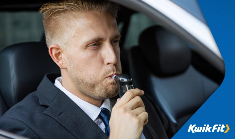 Person in a suit taking a breathalyser test whilst sitting in the drivers seat of a vehicle.